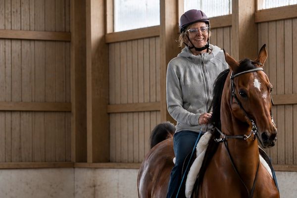 A woman wearing a helmet rides a horse indoors, smiling.
