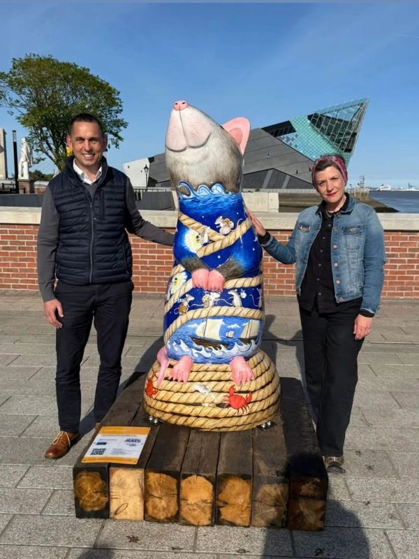 Two people standing beside a large, colorful rat sculpture outdoors.