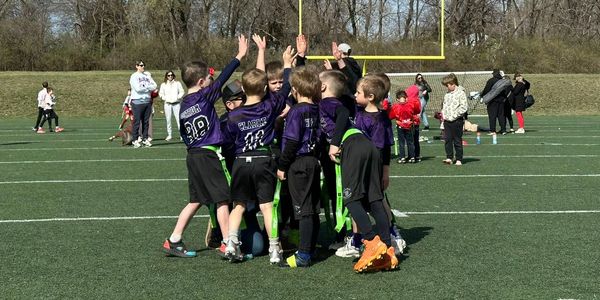 Kids in purple uniforms cheering on a football field.
