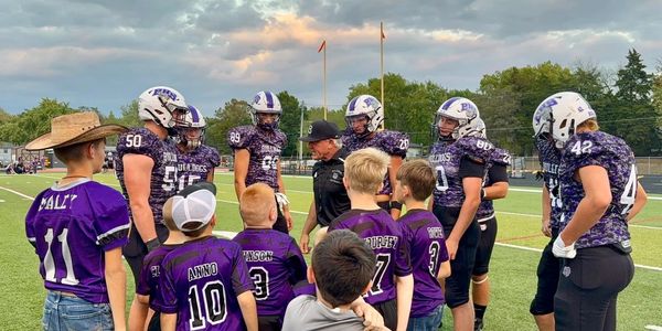 Football team huddling with kids on the field.