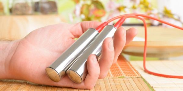 Person holding a jump rope with metallic handles and red rope.