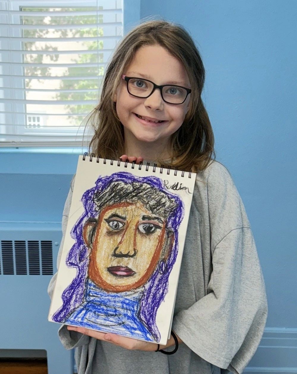 Young girl proudly holding a colorful self-portrait drawing.