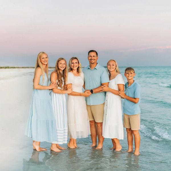 Family standing barefoot on the beach, smiling at the camera.