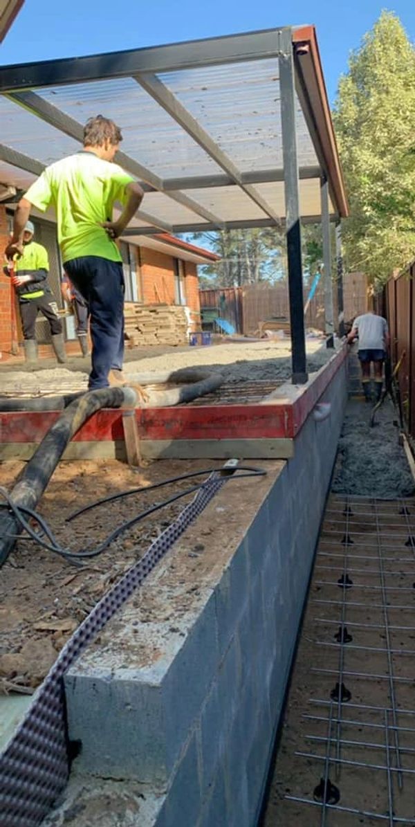 Team pouring concrete in a covered outdoor patio area beside front of the house 