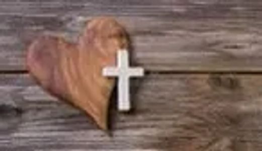 Wooden heart with a white cross on a rustic wooden background.