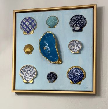 Framed art with decorated seashells on a blue background.