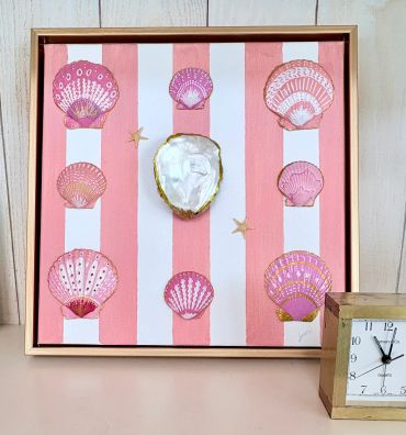 Framed artwork of seashells on pink and white stripes.