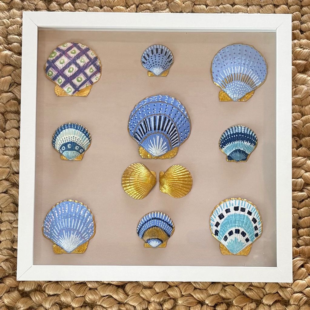 Framed collection of colorful seashell crafts on woven mat.