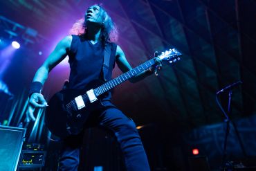 Guitarist passionately playing on stage under blue and purple lights.