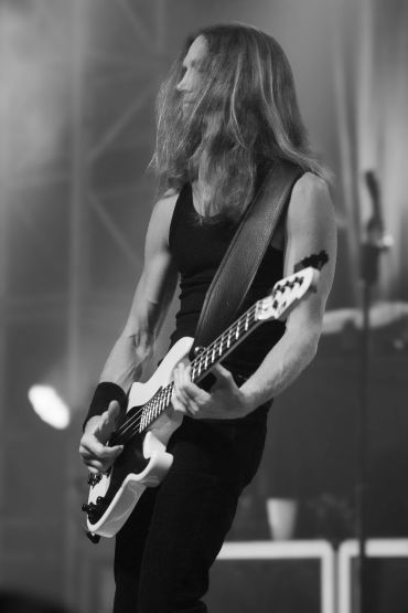 Long-haired musician intensely playing electric guitar on stage.