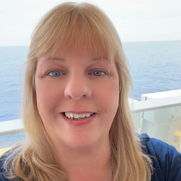 Smiling woman with blonde hair on a boat with ocean background.