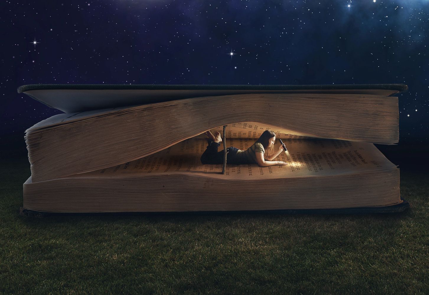 Girl with flashlight reading inside a book at night.