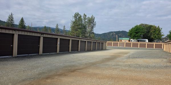 Outdoor storage unit complex with multiple closed brown garage doors under cloudy sky.