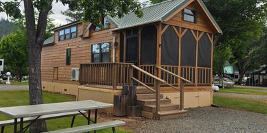 A wooden cabin with a screened porch surrounded by trees.