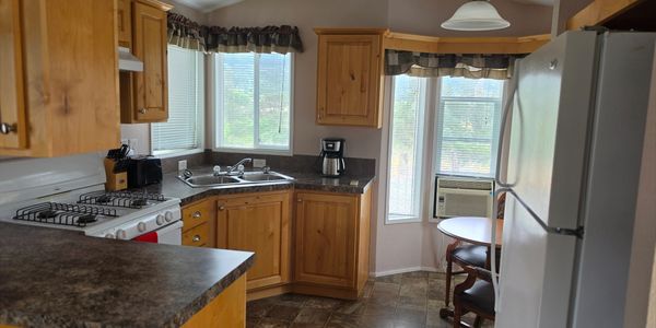 Cozy kitchen with wooden cabinets, marble countertops, and large windows letting in natural light.