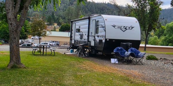 A parked RV with camping chairs and a picnic table in a scenic outdoor setting.