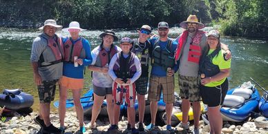 A group of eight people wearing life jackets standing on a rocky riverbank.