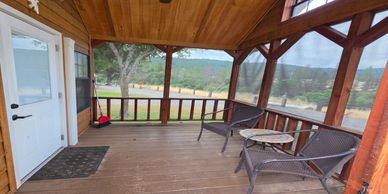 Wooden porch with two chairs and a small table overlooking a scenic landscape.