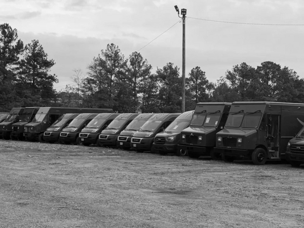 Row of black delivery vans parked on gravel under overcast sky.
