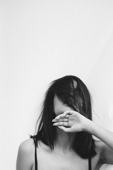 Woman with hair covering her face and hand raised.