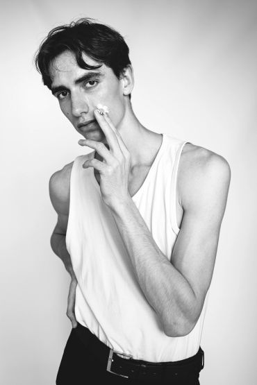 Young man in white tank top holding a flower to his face.