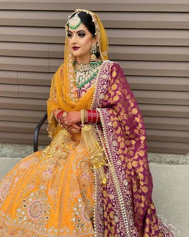 Bride in traditional vibrant orange and purple bridal attire with intricate embroidery and jewelry.