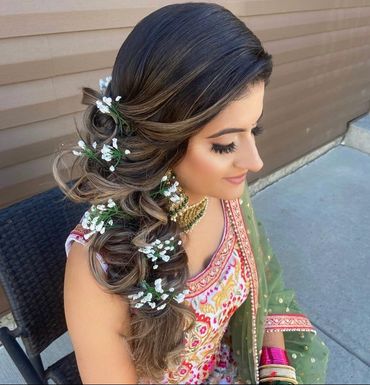 Woman with intricate braided hairstyle adorned with small white flowers, wearing traditional attire.
