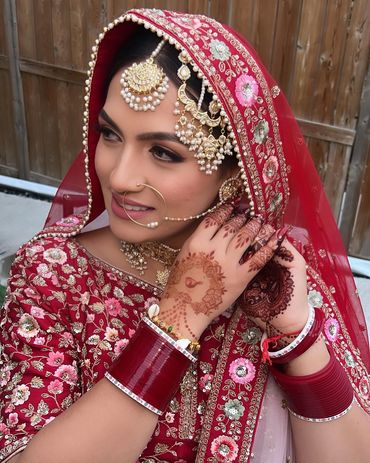 Bride in traditional red attire with intricate jewelry and henna designs.