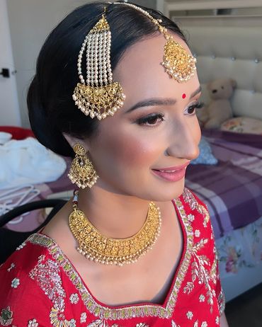 Bride in traditional red attire adorned with gold and pearl jewelry.