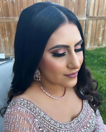 Woman with elegant makeup and traditional jewelry, wearing a detailed pink outfit.