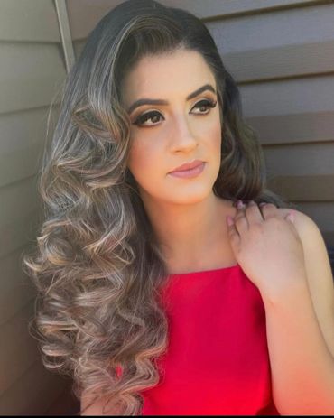 Woman with voluminous curly hair in a red top gazes thoughtfully.