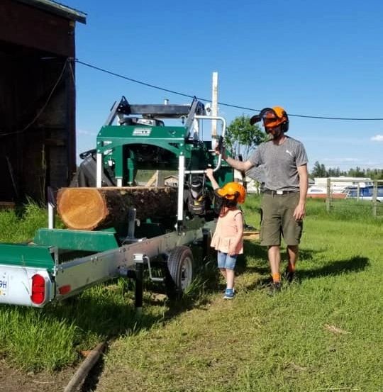 A man and child operating a log saw machine outdoors.