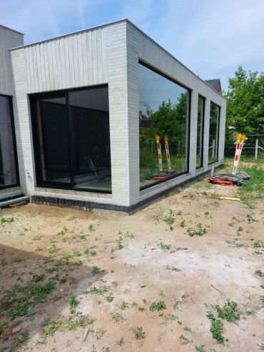 Modern huis met grote ramen en kale tuin.