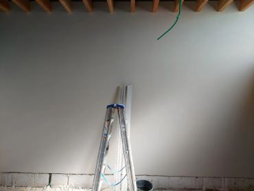 Schilderladder tegen een witte muur met onafgewerkte vloer.