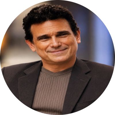 Man smiling in a dark blazer and ribbed sweater.