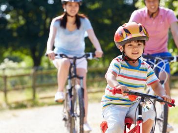 Child riding a bike with family outdoors.
