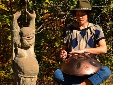 Photo of Sarah playing handpan beside a Buddha statue 
