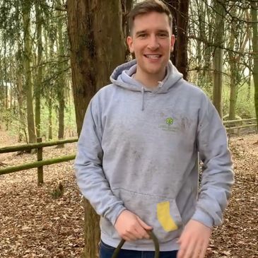 Chris Forest School Leader, in the woods wearing Little Sprout's Logo jumper, holding his dog's lead