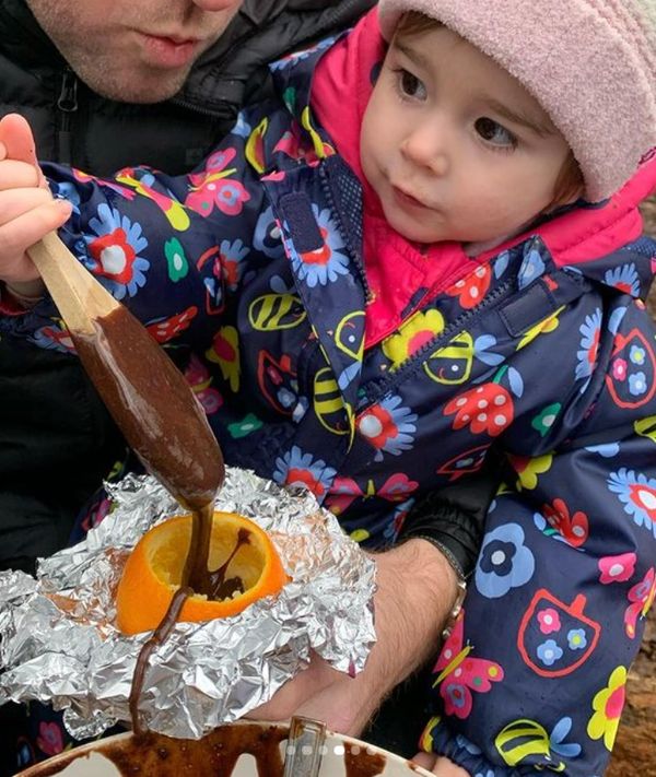 A child and parent spooning chocolate cake batter into a hollowed orange at forest school.
