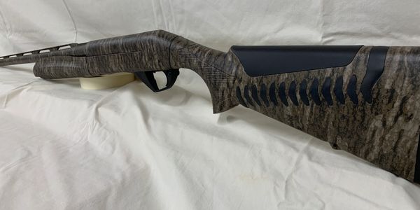 Camouflaged rifle lying on white fabric.