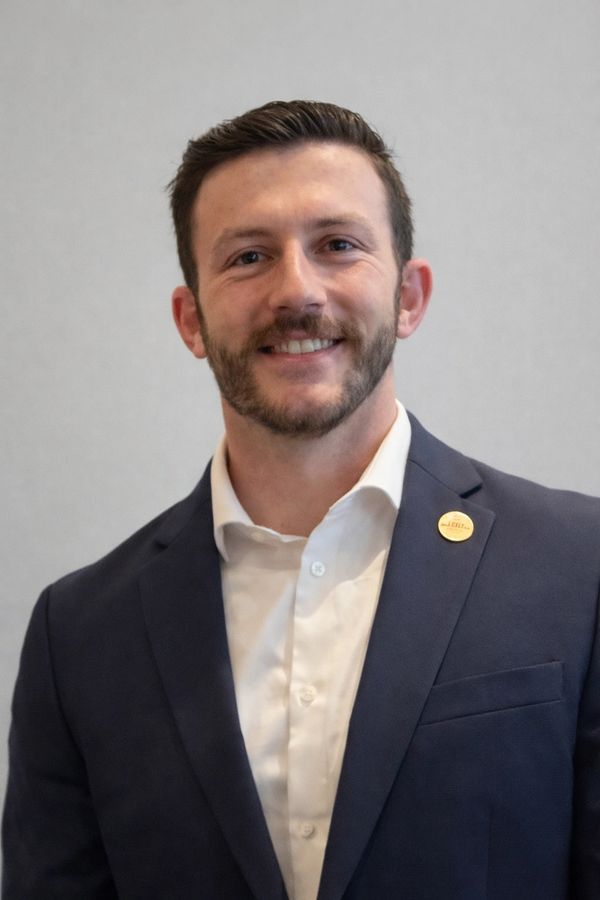 Smiling man in a navy blazer and white shirt.