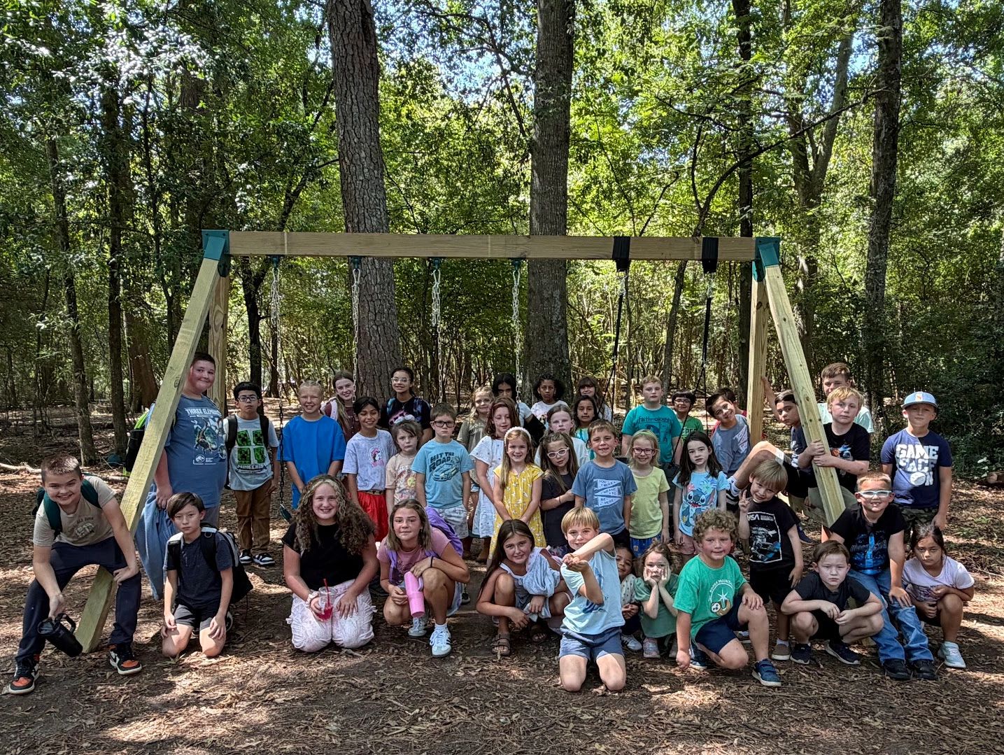Group photo of children at a wooded playground with swings.