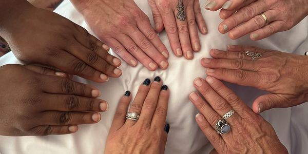 Six hands with different skin tones and rings together.