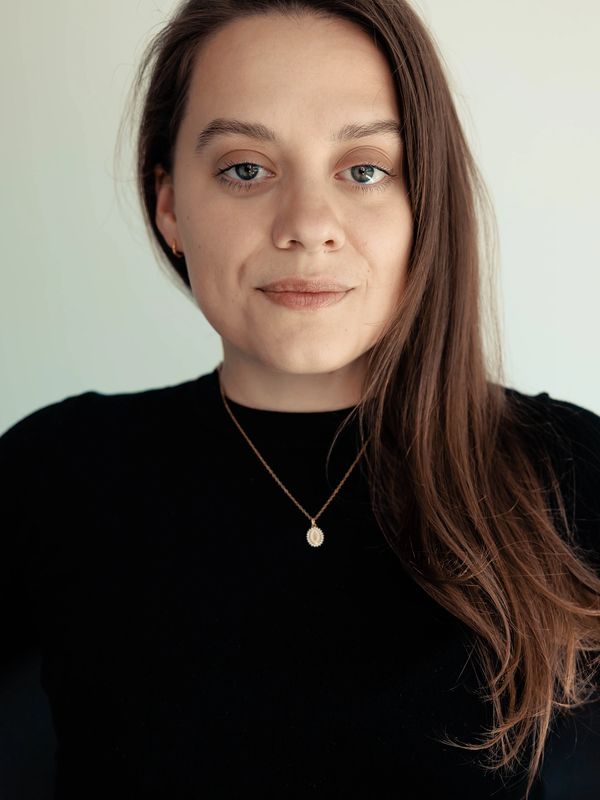 Young woman with long hair wearing a black top and gold necklace.