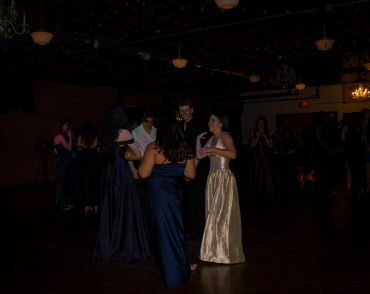 People dancing in a dimly lit room wearing formal dresses.