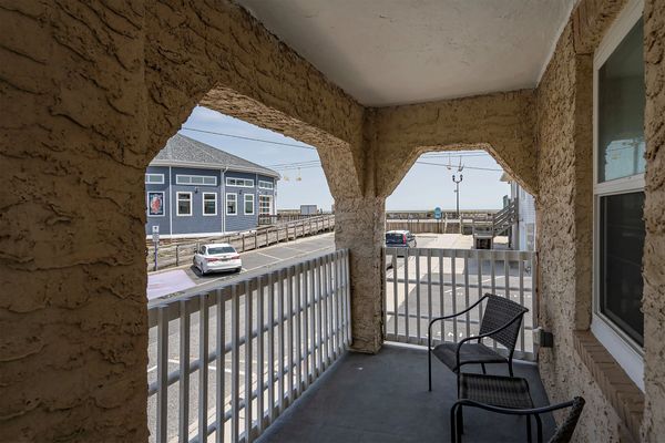 Balcony with two chairs overlooking a parking lot and a blue building near the beach.