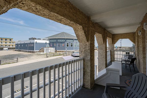 Covered balcony with chairs overlooking a street and blue building.