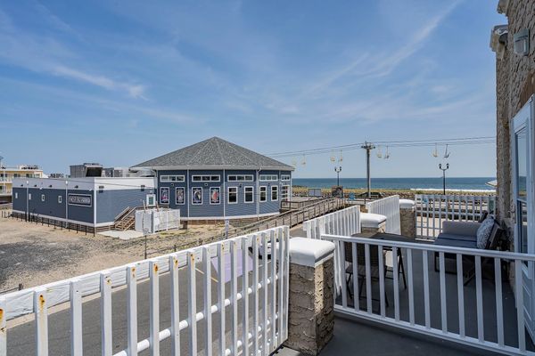 Balcony view overlooking a blue building and the ocean under a clear sky.