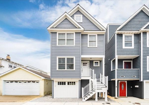 Modern gray townhouse with white trim and a front staircase under a partly cloudy sky.