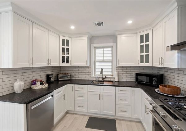 Modern white kitchen with black countertops and stainless steel appliances.